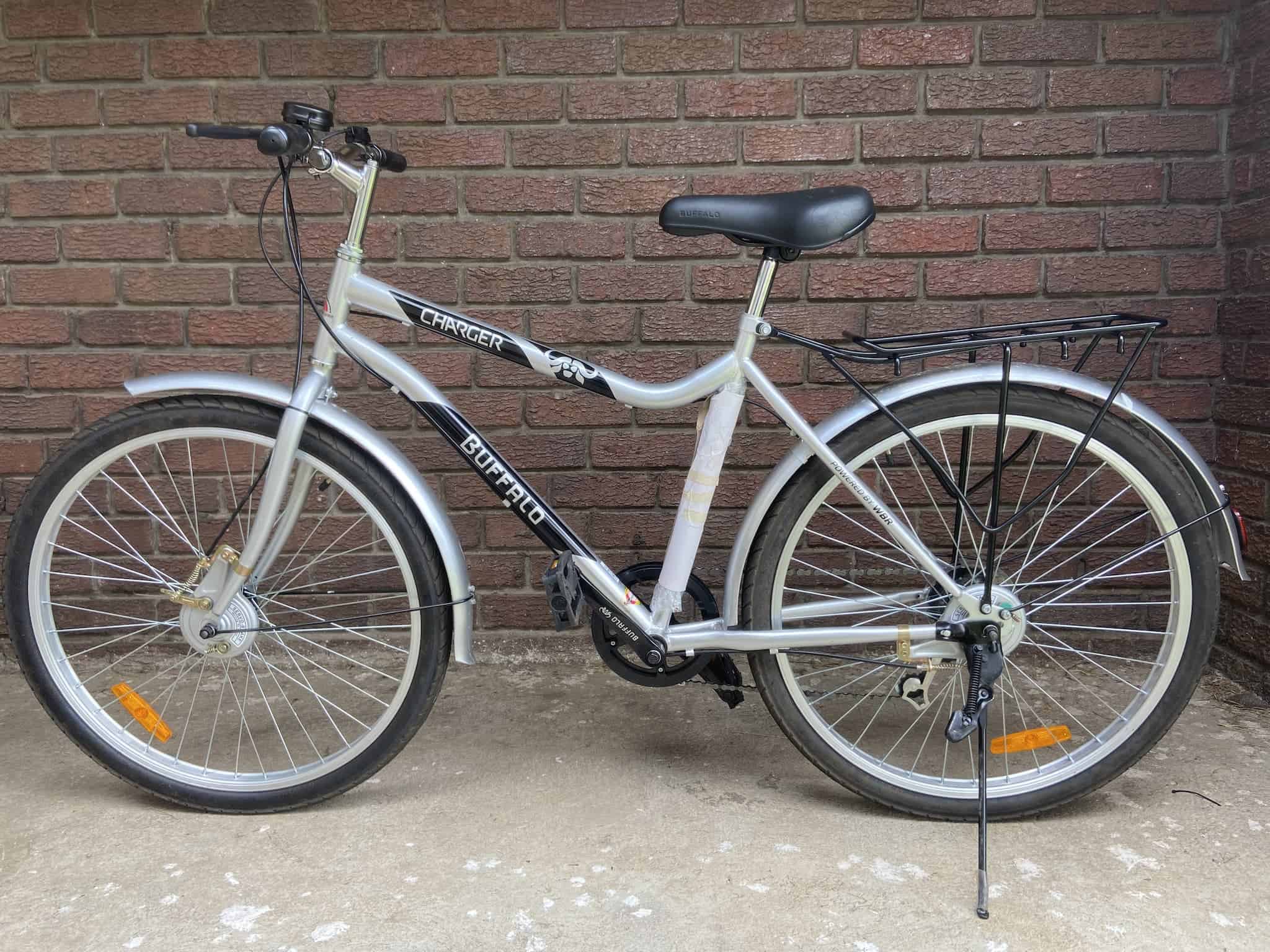 A silver bicyle with buffalo charger branding against a brick wall