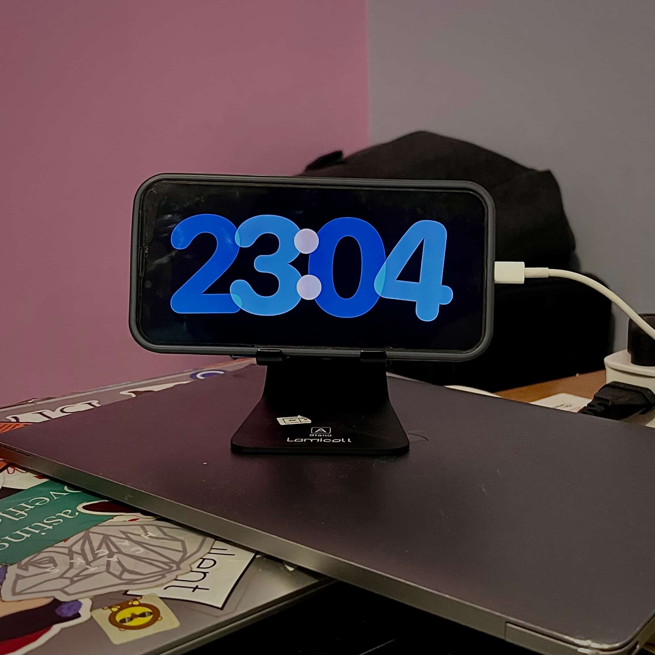 On top of two stacked laptops sits an iPhone resting on a stand horizontally with the time 22:04 in bubbly blue letters