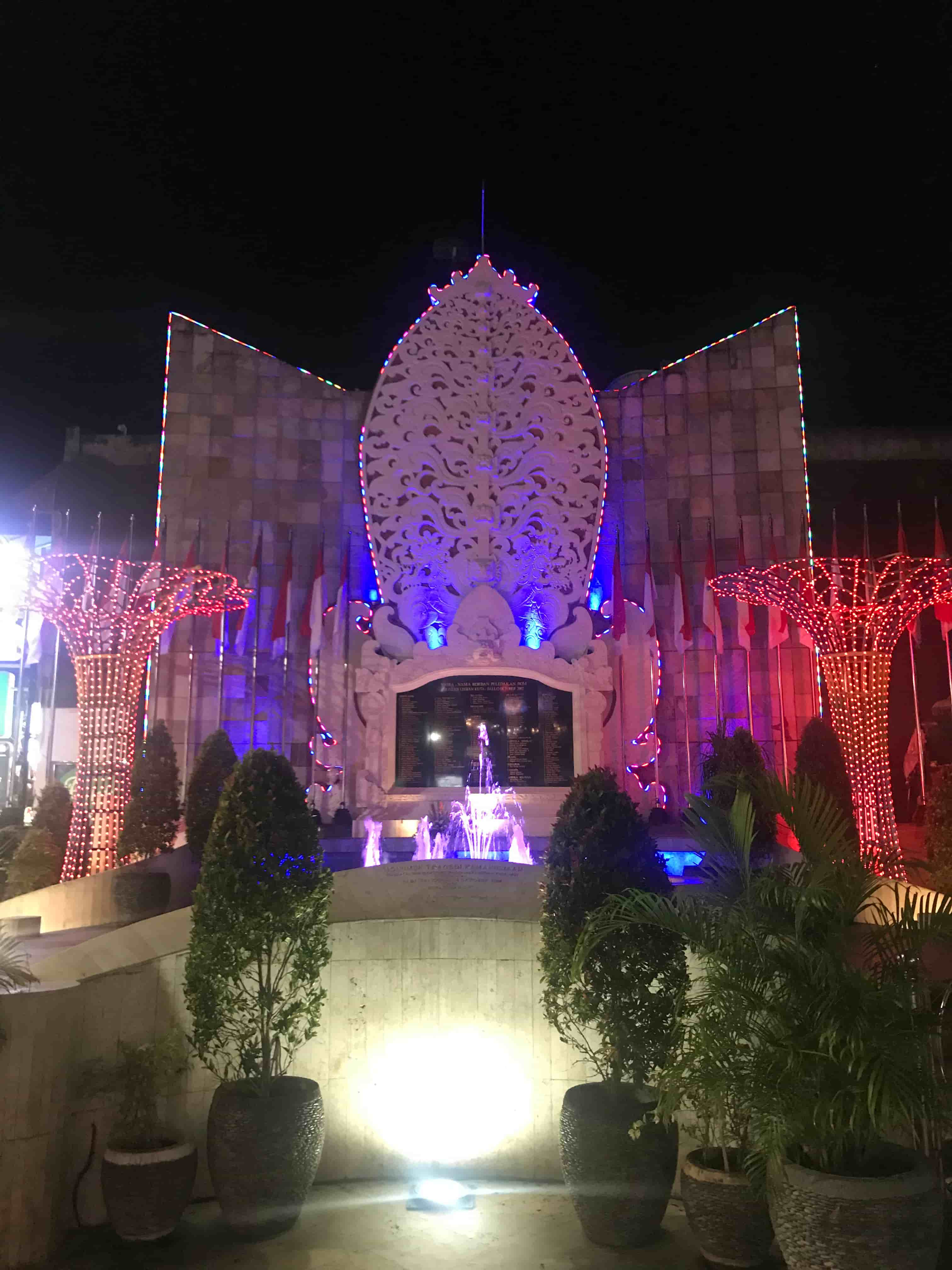 A large stone monument featuring the names of the victims surrounded by a landscaped garden and a fountain lit up at night