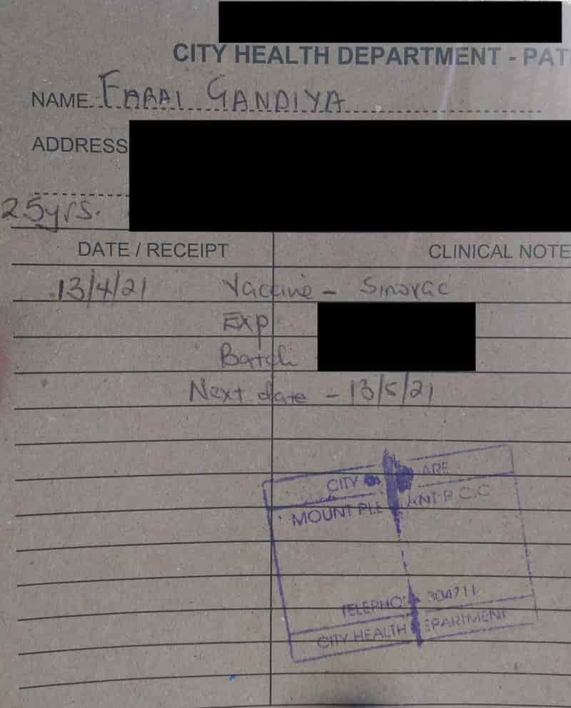 A torn khaki patient record card with my personal information (redacted), information on the vaccine dose (partly redacted) and the clinic’s stamp