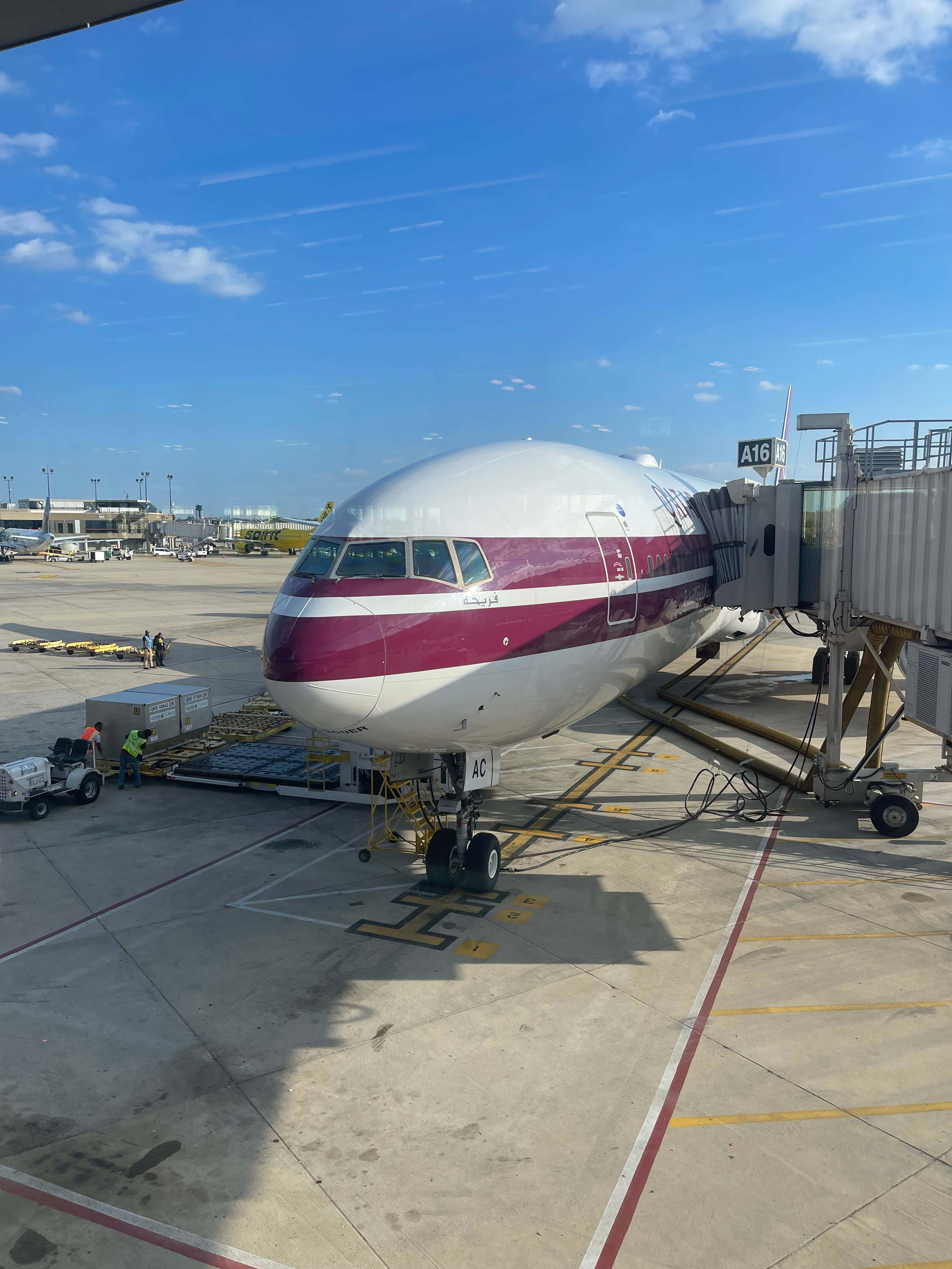 An off grey 777 with two maroon stripes at the boarding gate