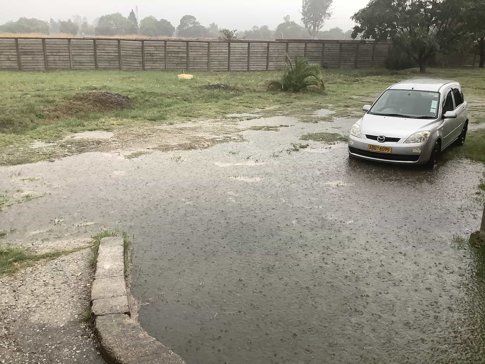 A yard with a car and puddles so big they’re practically a lake