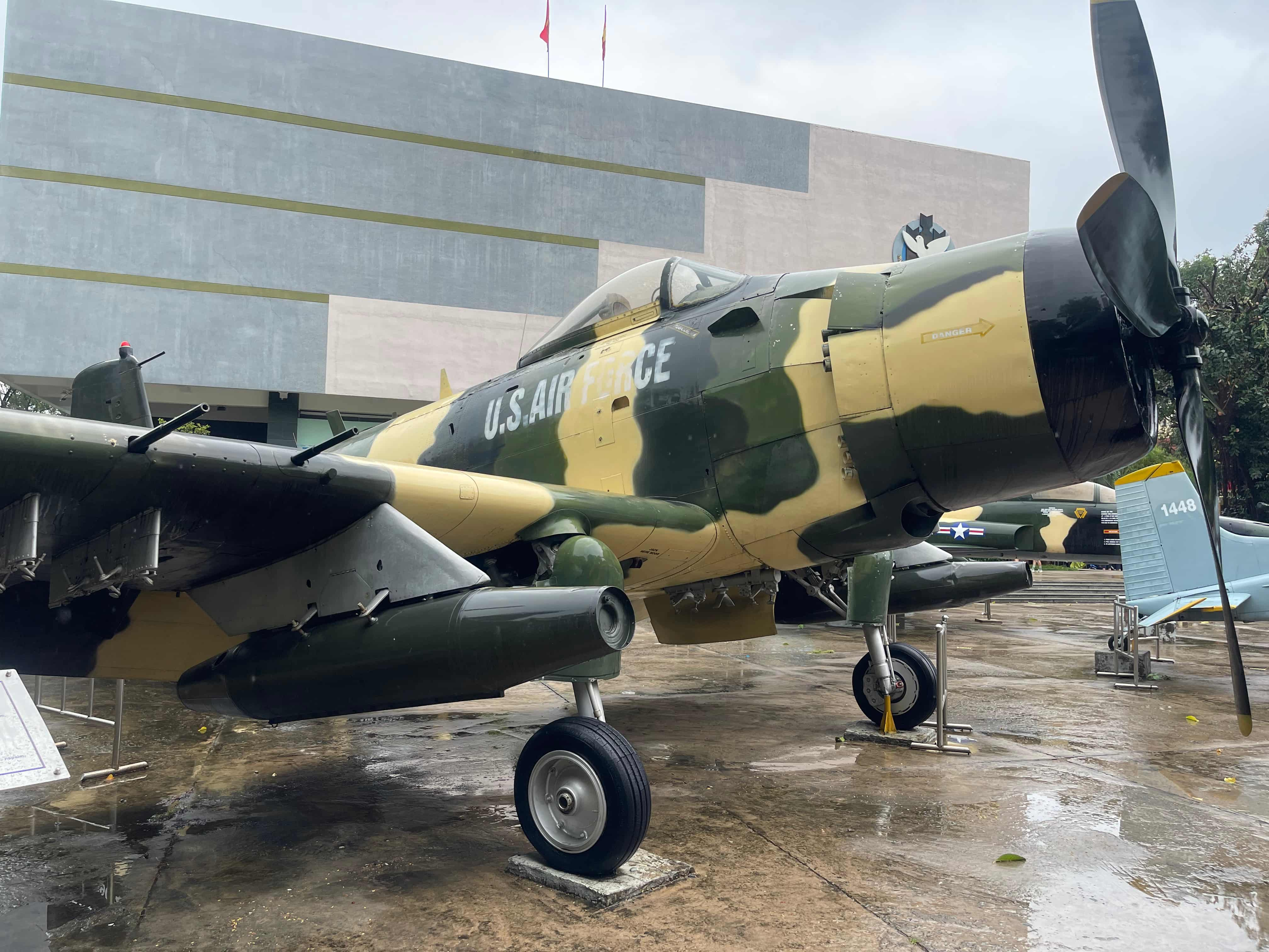 A US Air Force plane in camoflauge in the foreground against the modern War Remnants Museum building in the back