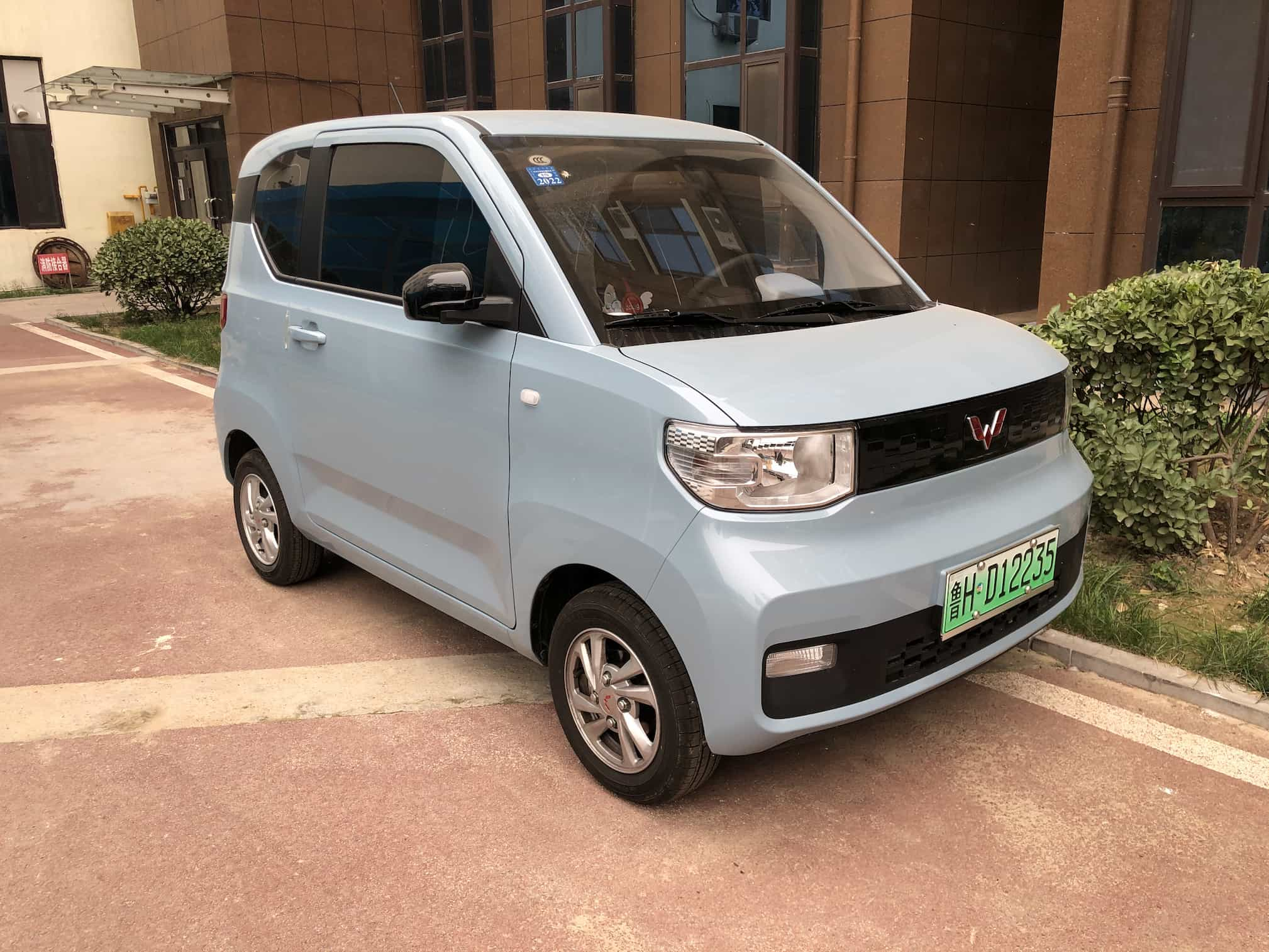 A light blue, boxy two-doored card parked outside a building