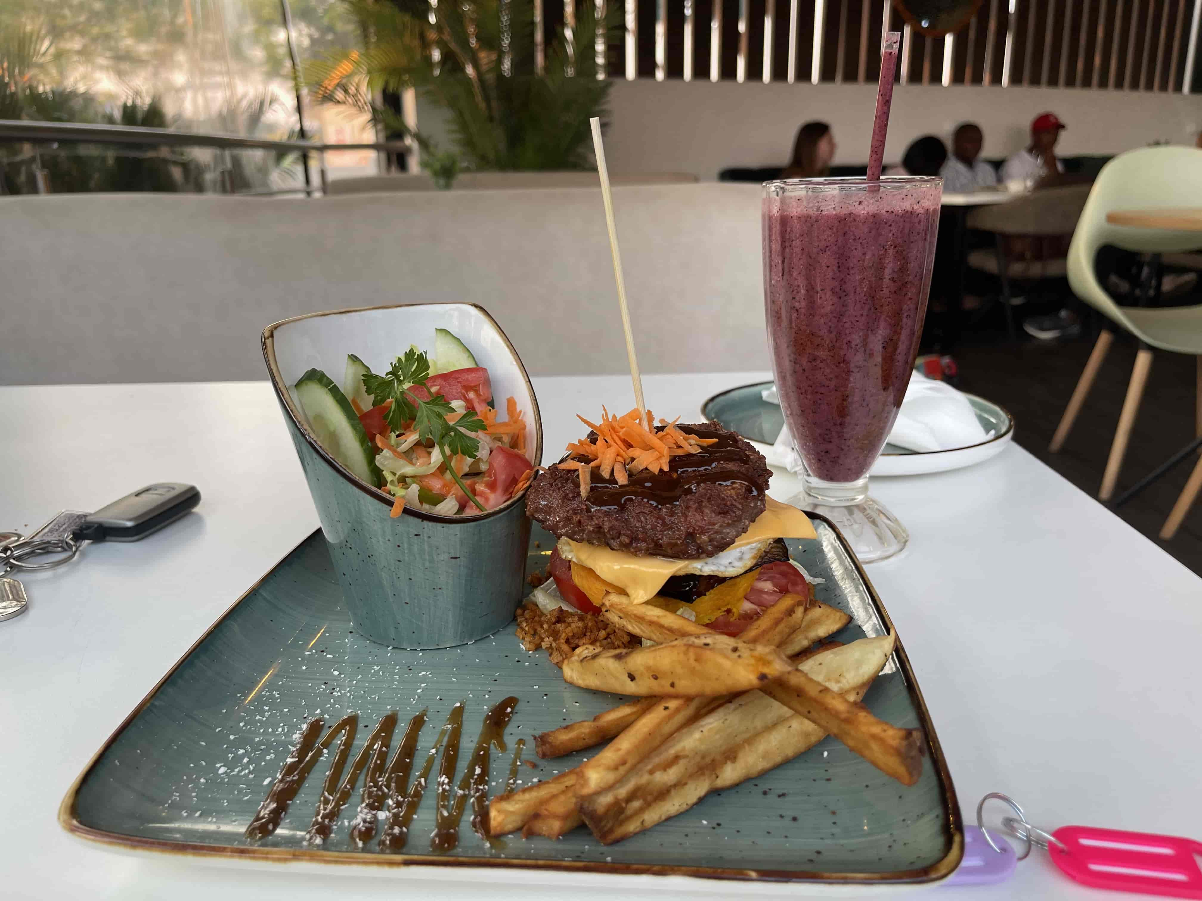 A full yet pattyless burger next to a garden salad, brown sauce and sweet potato fries. On the side is a purple smoothie.